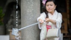 Chica con Kimono realizando la purificación en fuente de templo Shinto